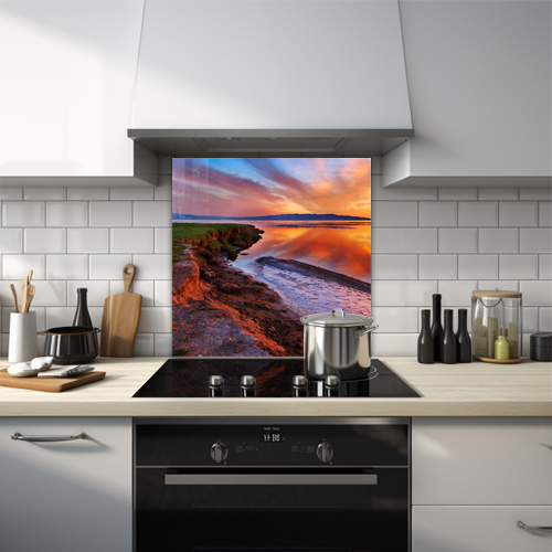 Sunset over a lake with a muddy bank and grass glass splashback.